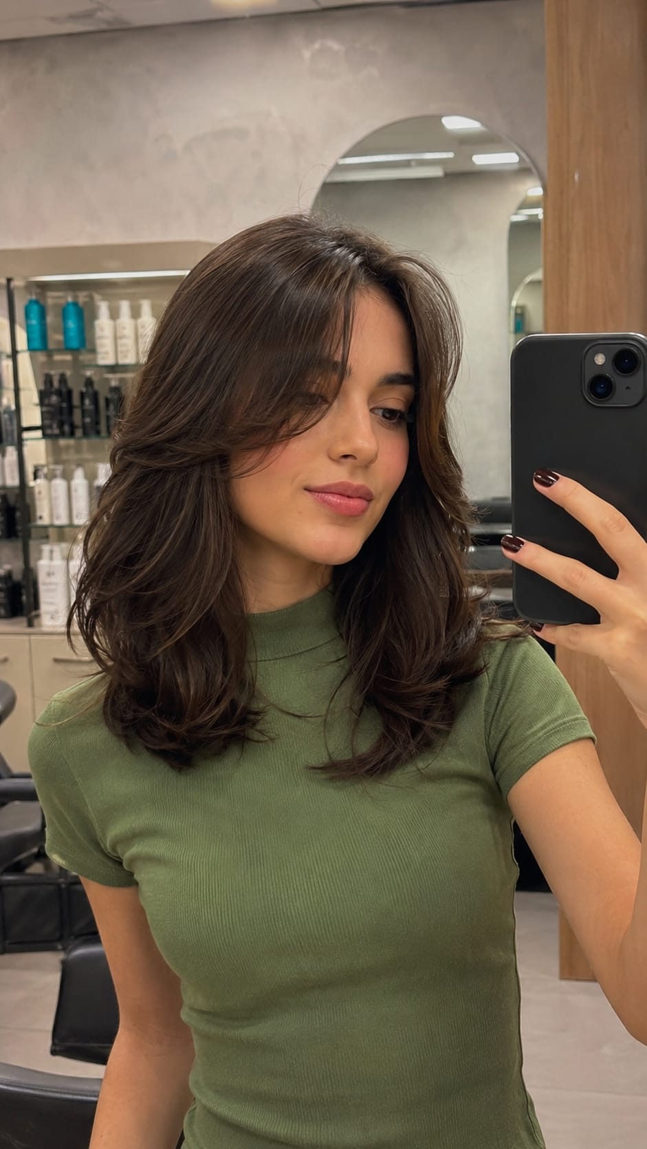 Mulher de blusa verde com curtain bangs tira selfie no espelho do salão